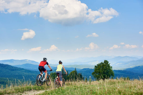 cyclists couple in professional sportswear and helmets on bicycles cycling cross country on  mountain road at bright sunny summer day, Active lifestyle and happy relations concept