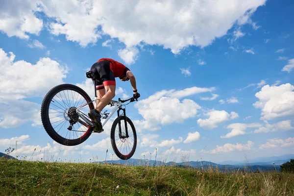 运动运动员骑自行车在专业运动衫和头盔跳跃骑脚踏车与天空和遥远的山在背景下 户外极限运动概念 — 图库照片