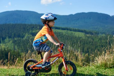 Verkhovyna, Ukrayna - 19 Ağustos 2017: Küçük sevimli okul öncesi çocuk kask ve şort ile T-shirt bisiklet çocuk 3 tekerlekli bisiklet çimenli Vadisi Dağları ile tarih ve zemin üzerine mavi gökyüzü