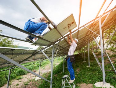Güneş Fotoğraf volta panelinin sistem kurulumu. Merdiven ve platform üzerinde duran iki teknisyen montaj ağır güneş paneli top. Yatırım alternatif enerji ve profesyonel inşaat kavramı.