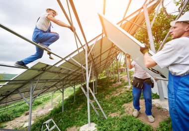 Güneş Fotoğraf volta panel sistem kurulumu. Üç teknisyenler ağır güneş pili yüksek üzerinde kaldırma. Yatırım alternatif enerji, para tasarrufu ve profesyonel inşaat kavramı.
