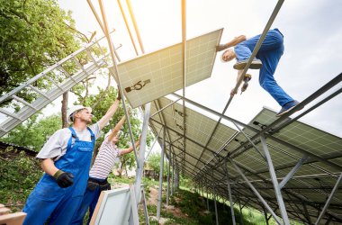 Tek başına güneş Fotoğraf volta panelinin sistem kurulumu. Aşağıdan ağır güneş paneli montaj üç teknisyen işçilerin görüntüleyin. Alternatif enerji üretim ve profesyonel inşaat kavramı.