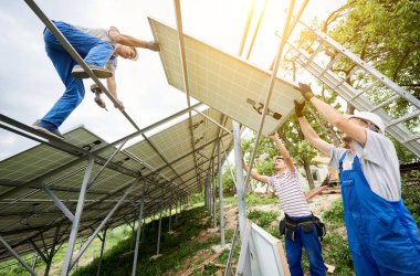 Tek başına güneş Fotoğraf volta panelinin sistem kurulumu. Aşağıdan ağır güneş paneli montaj üç teknisyen işçilerin görüntüleyin. Alternatif enerji üretim ve profesyonel inşaat kavramı.