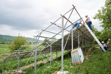 Tek başına güneş Fotoğraf volta panelinin sistem kurulumu. Aşağıdan ağır güneş paneli montaj üç teknisyen işçilerin görüntüleyin. Alternatif enerji üretim ve profesyonel inşaat kavramı.