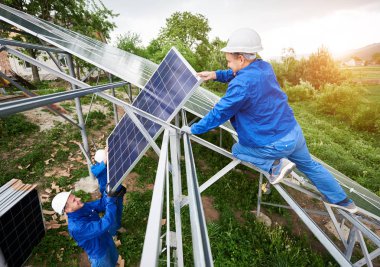Tek başına güneş Fotoğraf volta panel sistem kurulumu. Takım yeşil yaz görünümü arka plan üzerinde platformda güneş pili montaj hard-hats içinde üç teknisyenleri. Alternatif enerji kavramı.
