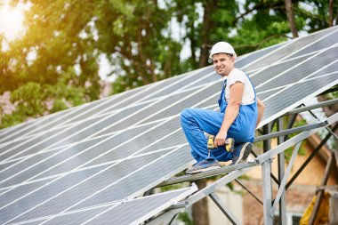 Neredeyse oturan genç gülümseyen elektrikçi işçi tek başına güneş Fotoğraf volta panel sistemi parlak güneşli yeşil ağaç arka plan üzerinde tamamlandı. Alternatif enerji kavramı.