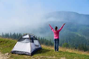 Etkin turist kız ile ayakta arkadan görünüm hill adlı turistik çadır, sisli dağlar manzarayı parlak yaz güneşli sabahı silah kaldırdı. Turizm ve seyahat kavramı. Karpat Dağları