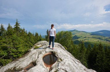 Ayakkabın Dağları'nın muhteşem manzarayı güzel mavi gökyüzü altında orta ile büyük kayanın üzerinde duran genç uzun saçlı turist kız arkadan görünüm hiç yeşil çam ormanları ile kaplı.