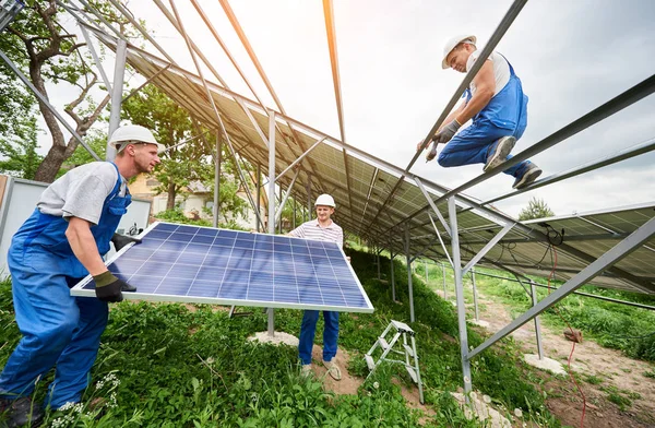 安装独立太阳能光电面板系统 三名技术员在高金属平台上举起大太阳模组 替代能源投资与专业建设理念 — 图库照片