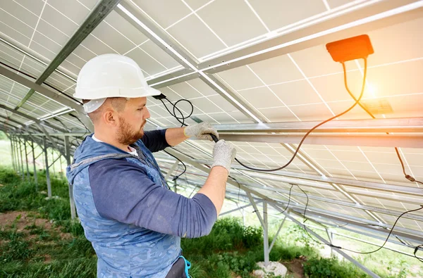 Installing and wiring of stand-alone solar photo voltaic panel system. Close-up of young electrician in hard-hat connecting electrical cables inside the solar modules. Alternative energy concept.