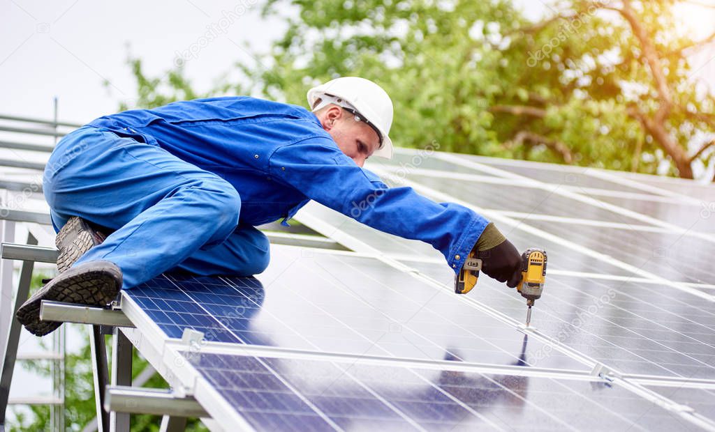 Young construction worker connects photo voltaic panel to solar system using screwdriver on bright sunny day. Alternative cheap sun energy production and profitable financial investment concept.