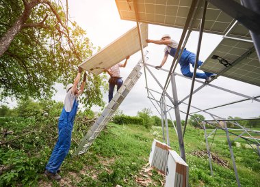 Tek başına güneş Fotoğraf volta panel sistem kurulumu. Üç teknisyen büyük güneş pili yüksek metal üzerinde kaldırma. Yatırım alternatif enerji ve profesyonel inşaat kavramı.