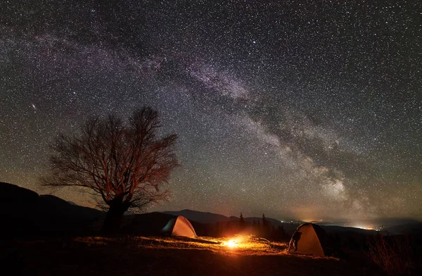 令人惊叹的夜间露营网站视图 明亮的篝火在两个旅游帐篷之间燃烧令人难以置信的美丽星空和银河 大树和遥远的山脉背景 — 图库照片