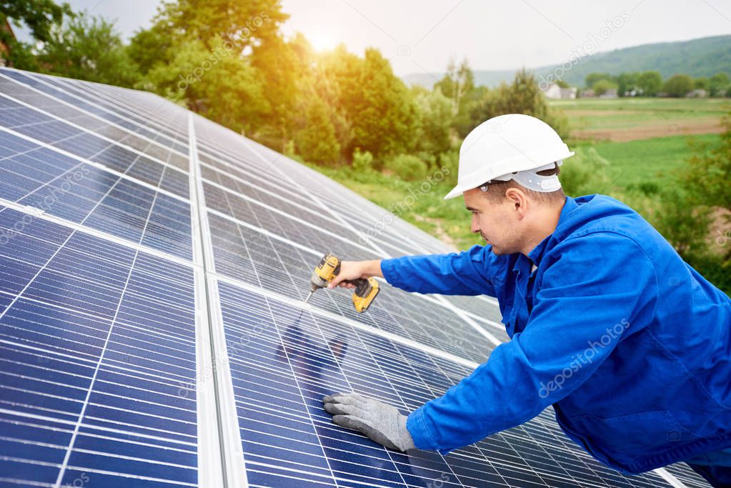 Construction worker connects photo voltaic panel to solar system using screwdriver. Professional installing and construction of solar system, alternative energy and financial investment concept.