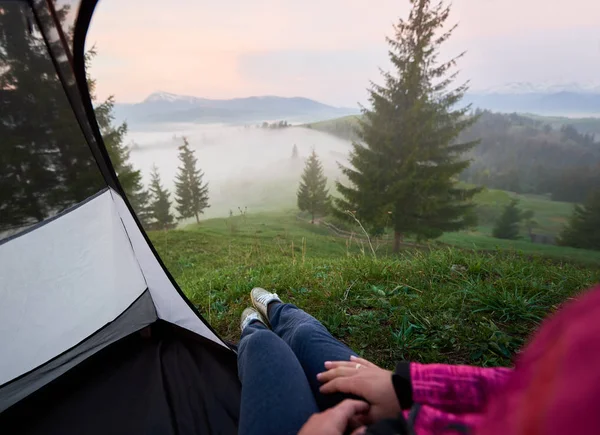 İlk plan sisli görünümü vadiler, çam ormanları ve kot pantolon ve spor ayakkabısı kadın bacaklar ile turist çadır içinde karlı tepe ile uzak Dağları. Turizm, kamp ve rekreasyon kavramı.