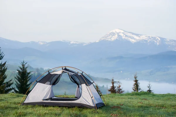 Çam ağaçları ve uzak dağ silsilesi karlı zirveleri ile arka çimenli tepeye açık boş küçük turistik çadırın sabah güneş tarafından yaktı. Turizm, kamp, rekreasyon ve doğa kavramının güzellik.