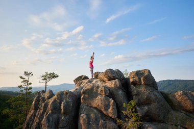 Çekici kız ile ayakta el yoga poz yeşil ağaç başında üzerinde kayalık dağ üstüne ve açık mavi gökyüzü arka planda yaz sabahı kaldırdı. Spor, yoga ve sağlıklı yaşam konsepti.