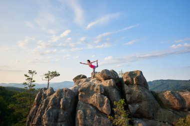 Karmaşık yoga poz yapıyor genç ince kadın tarafından büyük kaya yaz güneş top yeşil ağaç üstleri ve açık mavi gökyüzü arka plan üzerinde sabah yaktı. Fitness ve sağlıklı yaşam konsepti. Narajasana