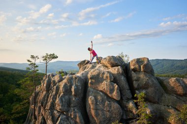 Çekici atletik kız buzlu yeşil dağlar ve açık mavi gökyüzü arka plan büyük kazık üzerine karmaşık yoga egzersizleri yapıyor. Tırmanma, turizm, fitness ve sağlıklı yaşam konsepti.