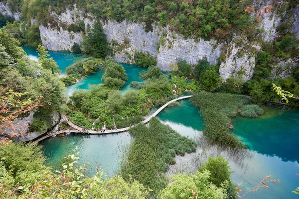 普利特维切湖国家公园 联合国教科文组织世界遗产中心 由太阳绿色森林在岩石峭壁和长的木桥梁点燃的空中看法与游人在湖用清澈的蓝色绿色水 — 图库照片