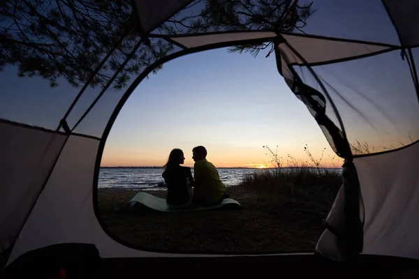 从旅游帐篷内查看 年轻的旅游情侣的剪影 男人和女人坐在湖岸边的蓝色傍晚的天空和水晶蓝色清澈的湖泊水背景 — 图库照片