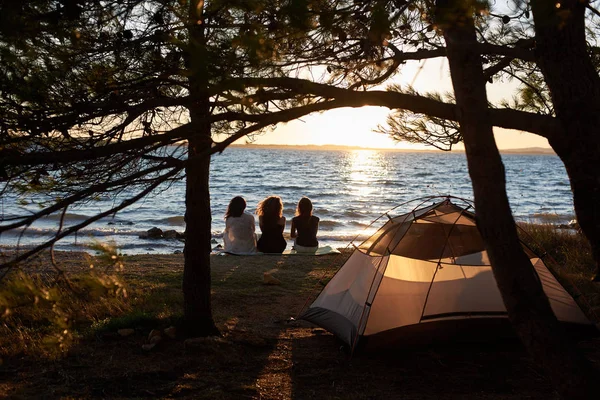 Bakifrån Tre Unga Kvinnor Sitter Sjöstranden Framför Turist Tält Träd — Stockfoto