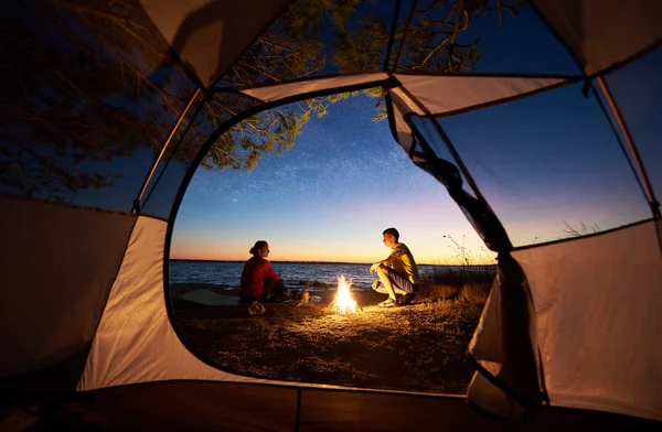 見る夕日観光テントの中 若い観光客ロマンチックな家族 男と女のたき火の夜の空とクリスタルの青い透明な湖水背景青湖岸に夕食を作りに座って — ストック写真