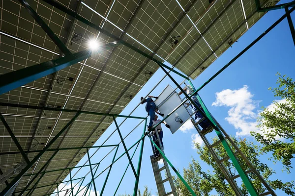 Tres montadores que sostienen paneles solares en construcción metálica alta . — Foto de Stock