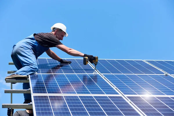 男は家の屋根に近代的な太陽電池を搭載します 高いはしごとプロのドリルを使用します 環境フレンドリーな緑エネルギー 生態学的です 自然再生可能エネルギーを使用しています 仕事の制服を着てください — ストック写真