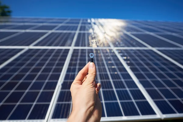 Man hand keeping tiny detail for solar battery installing in front of solar pannel on background.