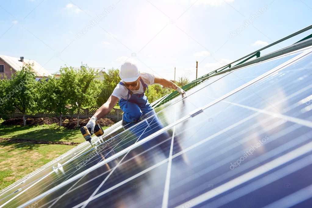 Worker mounting solar panels for renewable energy on house's roof. Using special equipment, wearing protective helmet. Environment friendly,resources saving, using renewable solar electricity.