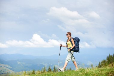 Sırt çantası ve güneş gözlüğü, çimenli tepeye yürüyüş Karpat dağ yolu, hiking kadın uzun yürüyüşe çıkan kimse gülümseyen trekking kullanarak, bulutlu gün yaz zevk yapışıyor. Açık hava etkinliği, turizm kavramı