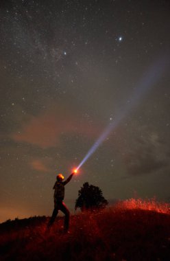 Elinde bir fenerle dağlarda gece yıldızlı gökyüzü karşı duran kadın silüeti