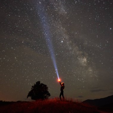 Elinde bir fenerle dağlarda Samanyolu ile gece yıldızlı gökyüzü karşı duran kadın silüeti