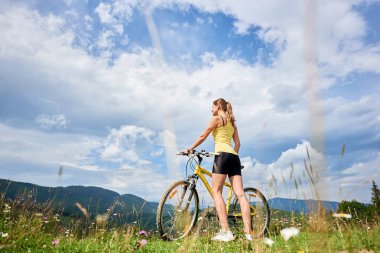 Arkadan sarı dağ bisikleti ile ayakta, dağlarda yaz günü zevk çekici mutlu kadın bisikletçi görünüşü. Açık spor aktivitesi, yaşam kavramı