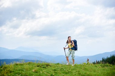 Sportif Karpat dağ yolu, hiking kadın backpacker sırt çantası, giyen çimenli tepeye yürüyüş gülümseyen trekking kullanarak, bulutlu gün yaz zevk yapışıyor. Açık hava etkinliği, yaşam kavramı