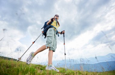Düşük açılı görünüş sırt çantası ve güneş gözlüğü, trekking, sopa yaz günü zevk kullanarak giyen çimenli tepeye yürüyüş dağ yolu, hiking sportif kadın turist. Açık hava etkinliği, yaşam kavramı