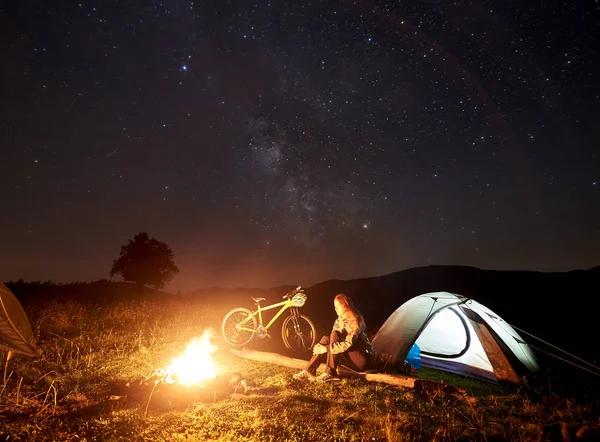 Ung Kvinna Cyklist Vilar Natten Camping Nära Brinnande Lägerelden Belysta — Stockfoto