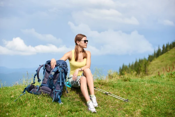 Güneş gözlüğü, Karpat Dağları yaz günü zevk takıyor, sopa trekking oturan ve sırt çantası ile çimenli tepe üzerinde dinlenme çekici mutlu kadın backpacker. Açık hava etkinliği, turizm kavramı