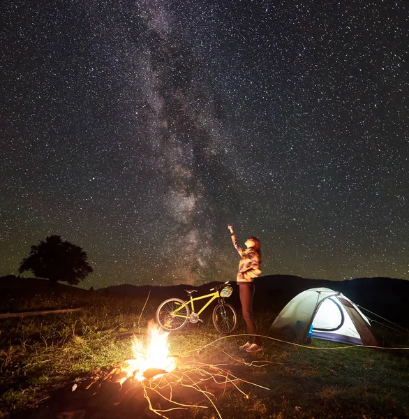 Genç kadın turist kamp, inanılmaz güzel bir akşam gökyüzü yıldızlar ve Samanyolu dolu işaret, kamp ateşi, ışıklı çadır, dağ bisikleti yanan yakın duran gece dinlenme. Turizm kavramı