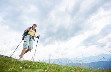 Sırt çantası ve güneş gözlüğü, trekking, sopa yaz günü zevk kullanarak giyen çimenli tepeye yürüyüş dağ yolu, hiking çekici kadın fiyatı düşük açılı görünümü. Açık hava etkinliği, yaşam kavramı