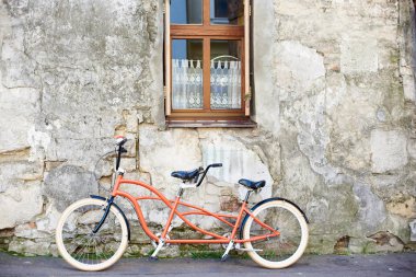 Modern rahat turuncu tandem çift kişilik bisiklet beyaz tekerlekli için dantel perde ile eski sıvalı kırık vintage house duvar üzerinde küçük temiz pencere parlak güneşli yaz gününde eğildi.