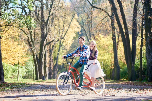 年轻的游客夫妇 英俊的胡子男子和迷人的金发长发女子在眼镜骑自行车一起串联双红色自行车与金色的树叶在高大的树木背景 — 图库照片