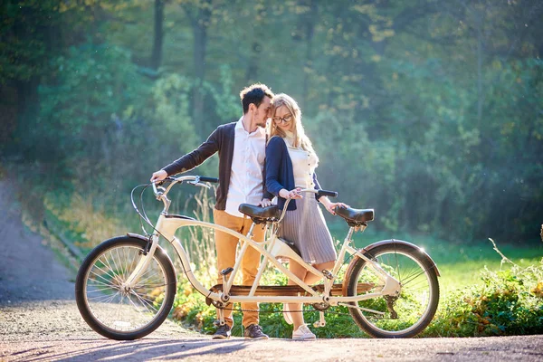 年轻幸福浪漫的情侣 胡子男子和迷人的女人紧密在一起在夏季公园或森林在阳光明媚的绿色树木茂密的树叶背景的双联自行车户外 — 图库照片