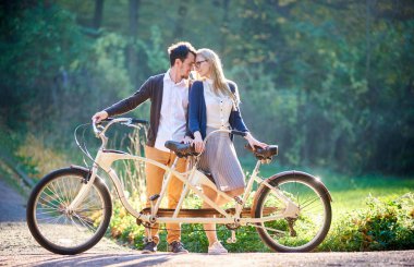 Romantik Çift genç güzel, açık havada yaz park veya orman içinde iki kişilik Çift kişilik bisiklet, sakallı adam ve çekici kadın birbirine yakın güneşli yeşil ağaçlar yoğun yeşillik arka plan bulanık..