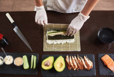 Usta bir suşi Nori ile rulo yapmak, mat pirinç, salatalık ve bambu kullanarak omlet. Yakın çekim işlemi bir bakış. En baştan görüntülemek