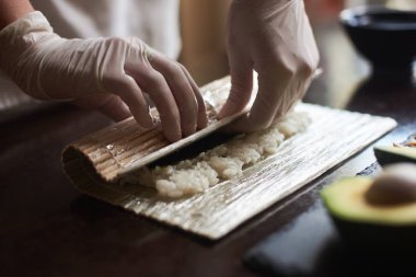 Master' s eller bir suşi nori ile rulo yapmak, mat pirinç, salatalık ve bambu kullanarak omlet. Yakın çekim görünümü sürecinin.