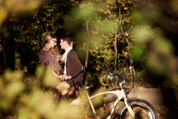 幸福浪漫的情侣 胡子男人和迷人的女孩紧密在一起的双自行车在秋季公园户外在阳光明媚的清理晚上在模糊的金色绿色散景背景 — 图库照片
