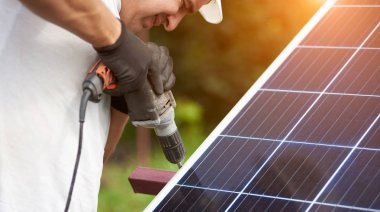 Yakın çekim bölüm görünümü profesyonel işçinin koruyucu eldiven güneş Fotoğraf volta paneli metal platformu bulanık yeşil yaz özgeçmişlerine kablolu Elektrikli tornavida kullanarak bağlanma.