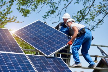 İki Genç teknisyen yeşil üzerinde uzun boylu çelik platformda ağır güneş Fotoğraf volta panel montaj arka plan ağaç. Dış güneş paneli Volta sistemi kurulması, tehlikeli bir iş kavramı.